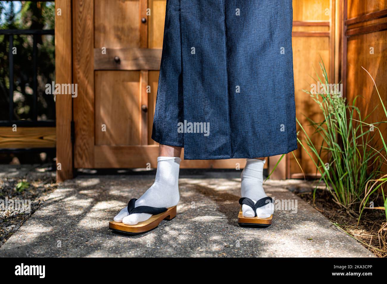 Erdgeschossansicht von Herrenfüßen in Kimono-Kostümen, geta tabi Schuhe Socken im Garten im Freien in Japan durch moderne hölzerne Tür Stockfoto