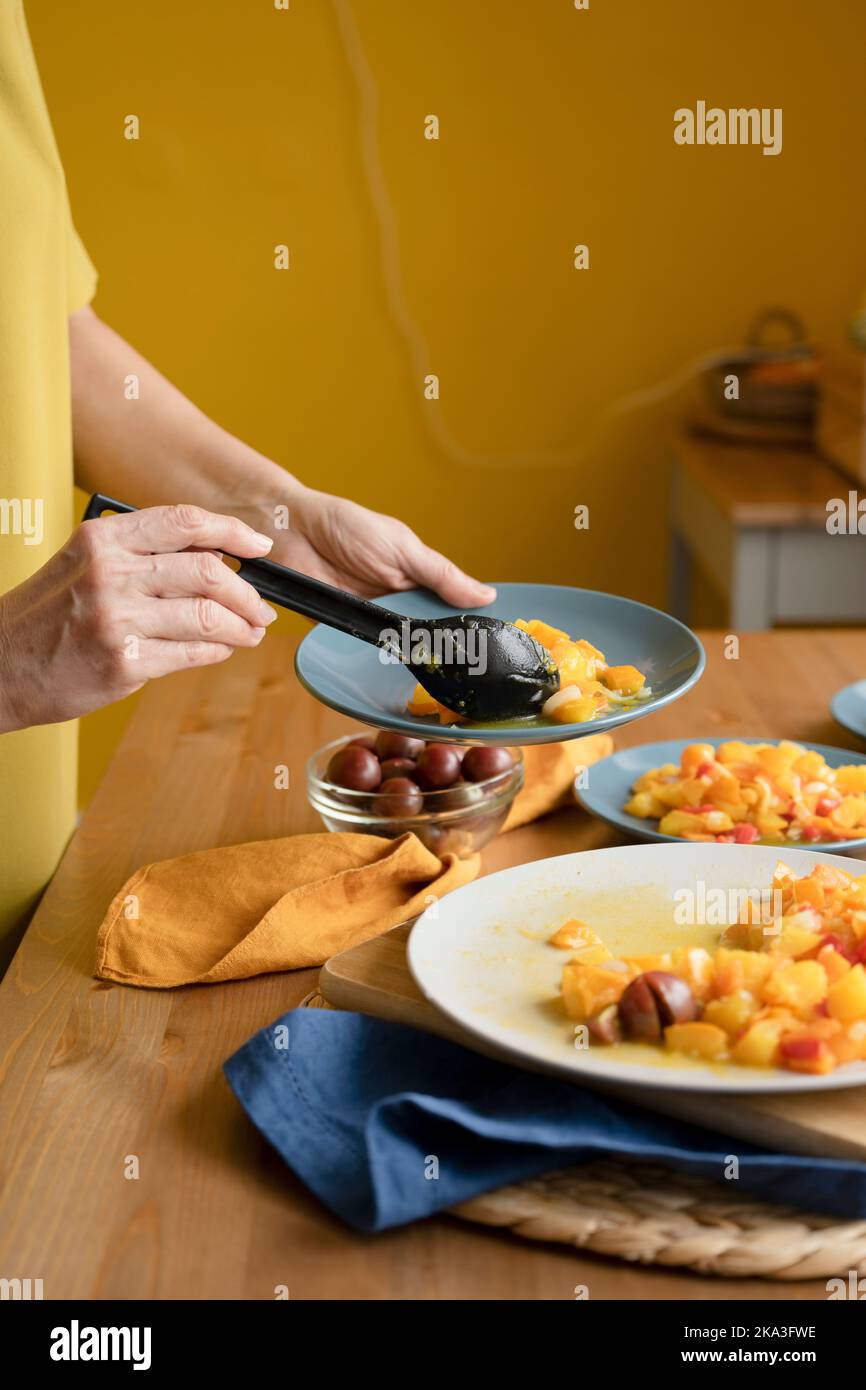 Crop anonyme Frau Putting leckere gesunde hausgemachte Gericht mit Kürbis und Tomaten auf den Teller stehen am Tisch in der Küche Stockfoto