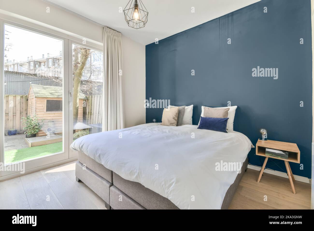 Komfortables Bett mit weichen Kissen in der Nähe der Tür, die zum Hinterhof in einem modernen Haus führt Stockfoto