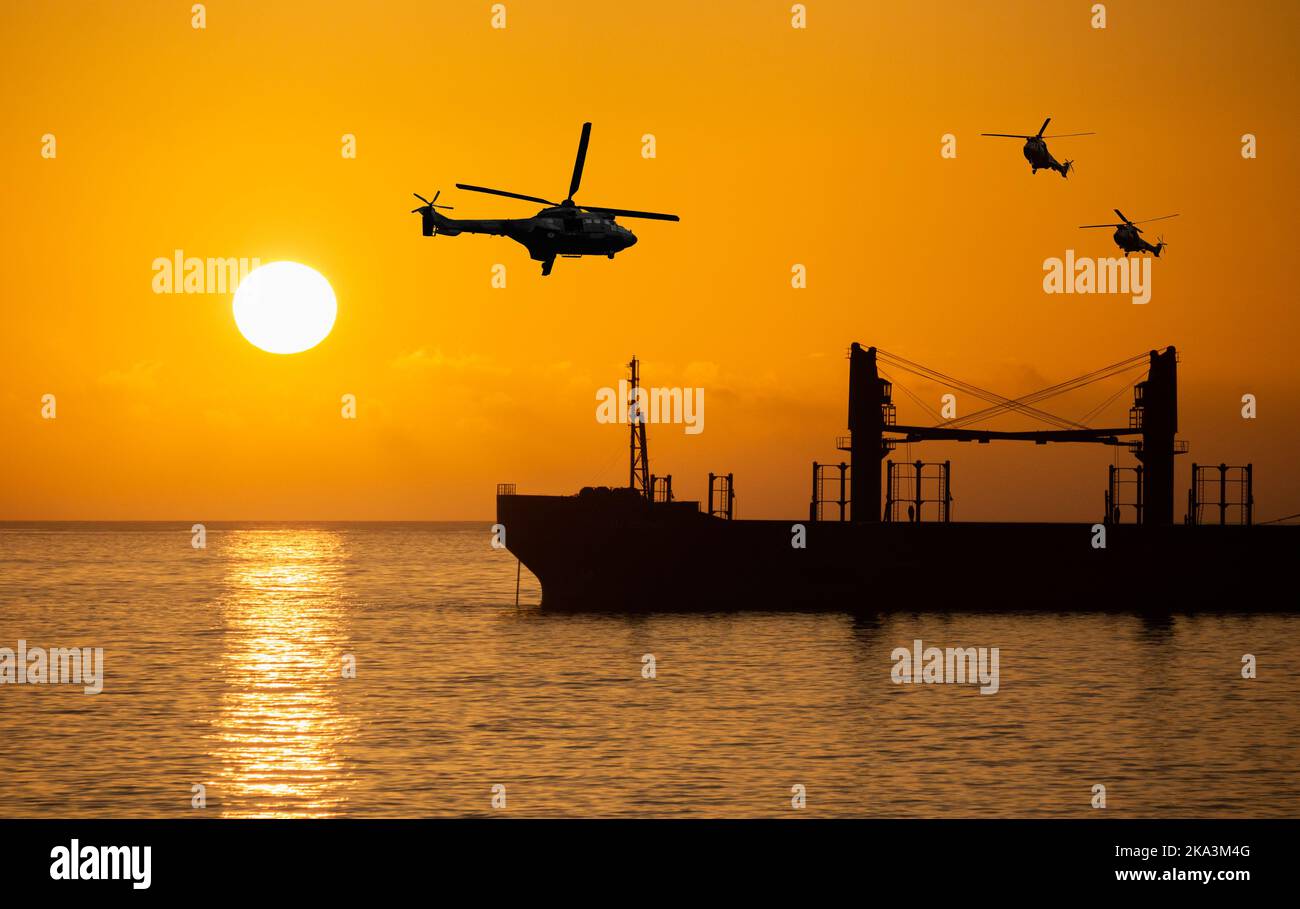 Militärhubschrauber über Massenfrachtschiff bei Sonnenaufgang. Ukraine Getreide, Weizen, Russland, Russlandkrieg, Lebensmittelblockade, Versand, Lebensmittelpreise angreifen.. Konzept Stockfoto