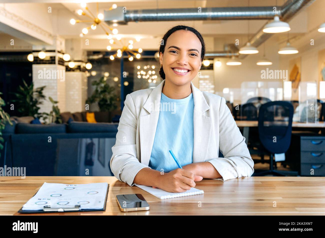 Schöne junge brasilianische oder latino erfolgreiche Frau, Business-Mentor, Finanzberater, Student, Blick auf Webcam während der Konsultation oder Webinar per Videokonferenz, Notizen im Notebook, lächelnd Stockfoto