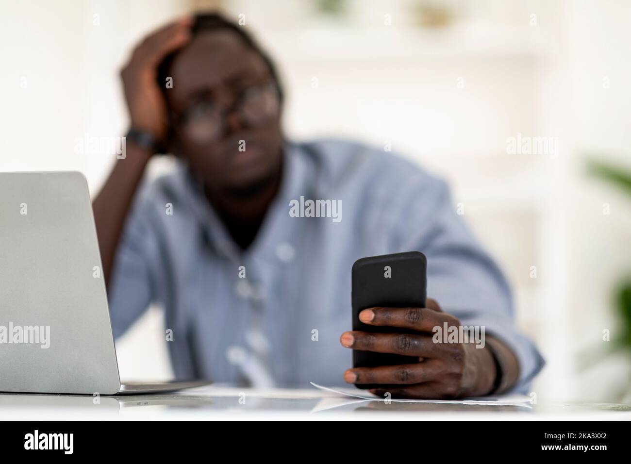 Junger Afroamerikanischer Mann Mit Smartphone, Während Er Am Schreibtisch Im Büro Sitzt Stockfoto
