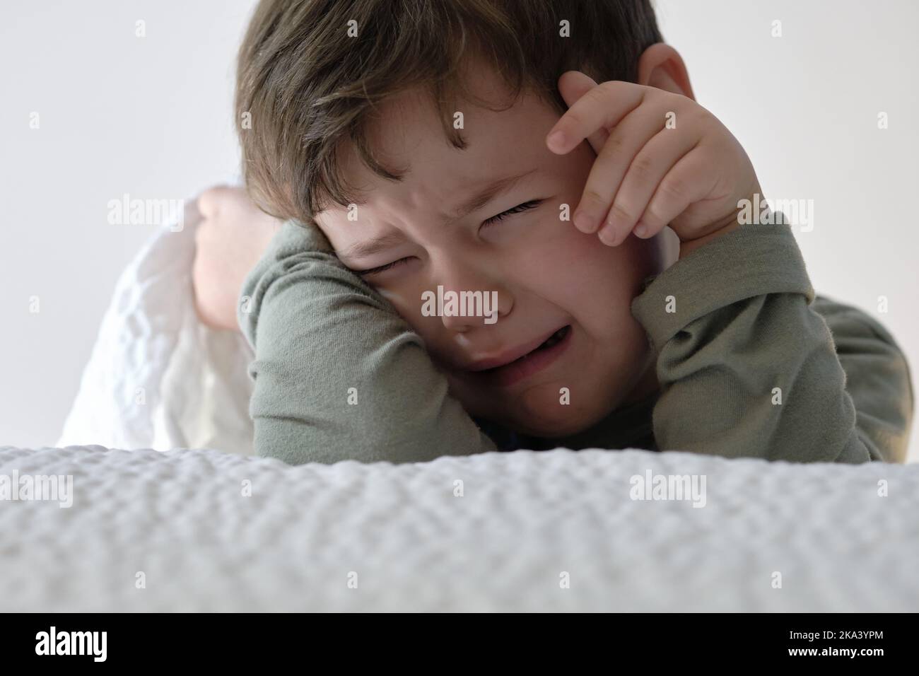Niedliches junges Kleinkind weint neben dem Bett Stockfoto
