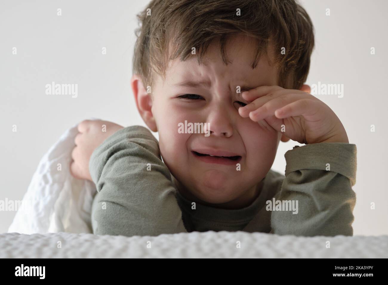 Niedliches junges Kleinkind weint neben dem Bett Stockfoto