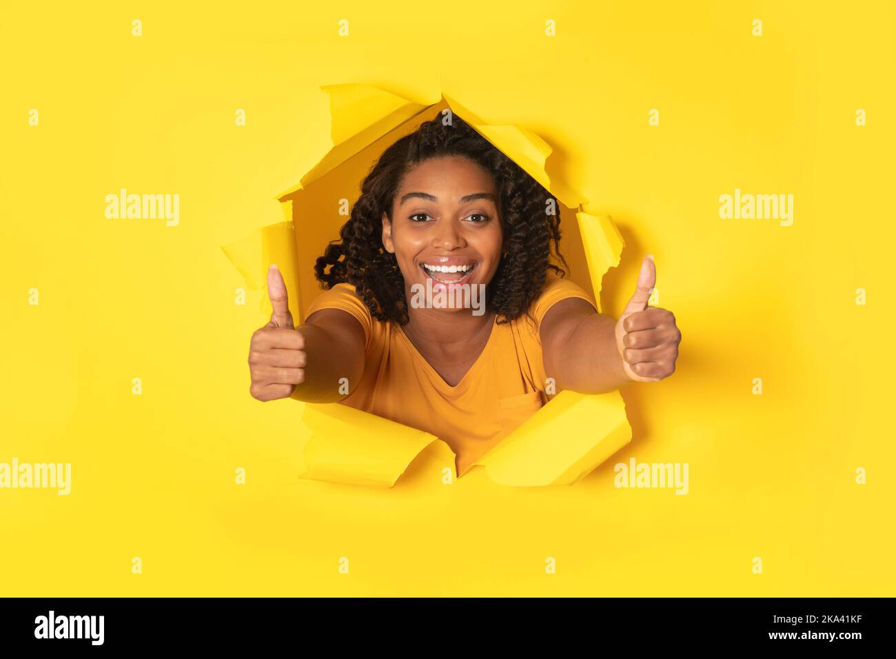 Schwarze Dame Gestikuliert Die Daumen Durch Zerrissenes Papier, Gelber Hintergrund Stockfoto