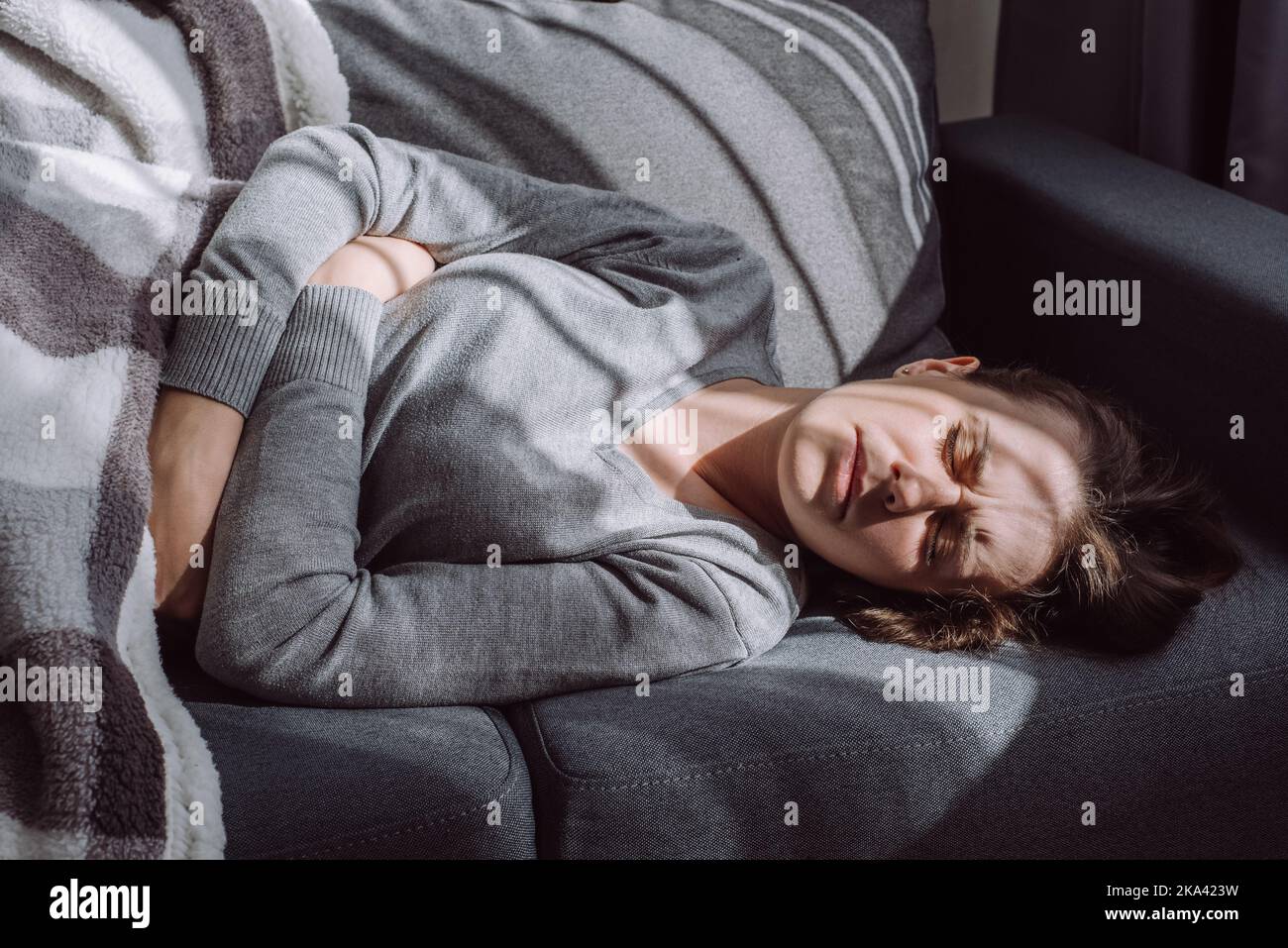 Ungesunde Frauen kämpfen mit schmerzhaften Schmerzen, die zu Hause auf der Couch liegen. Traurige, unglückliche junge Frau, die an Menstruationsschmerzen leidet, sich krank fühlt zu Magen, ho Stockfoto