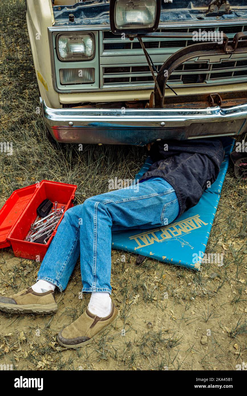 Mann auf dem Boden, der an einem alten Pickup-Truck mit Kopf und Schultern unter dem Fahrzeug arbeitet. Stockfoto