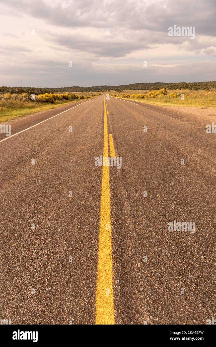 Zweispurige Asphaltautobahn im Norden von New Mexico ohne Autos auf der Straße, deutliche gelbe Linie in der Mitte. Stockfoto