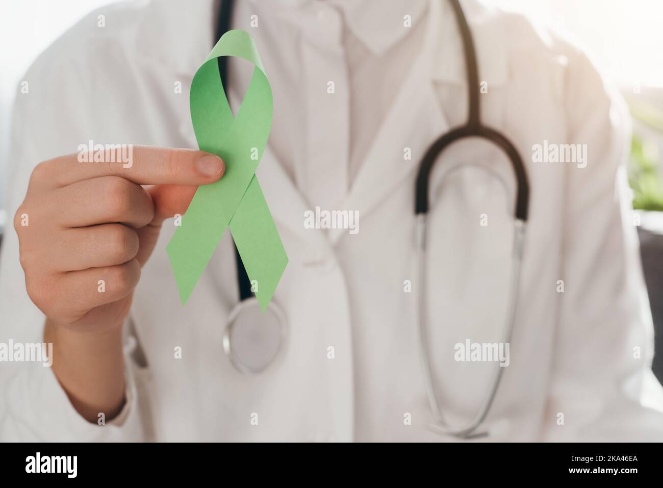 Nahaufnahme einer Ärztin im weißen Mantel mit Stethoskop, das ein lindgrünes Band auf der Couch hält, Bewusstsein für psychische Gesundheit, Welttag für psychische Gesundheit, Stockfoto