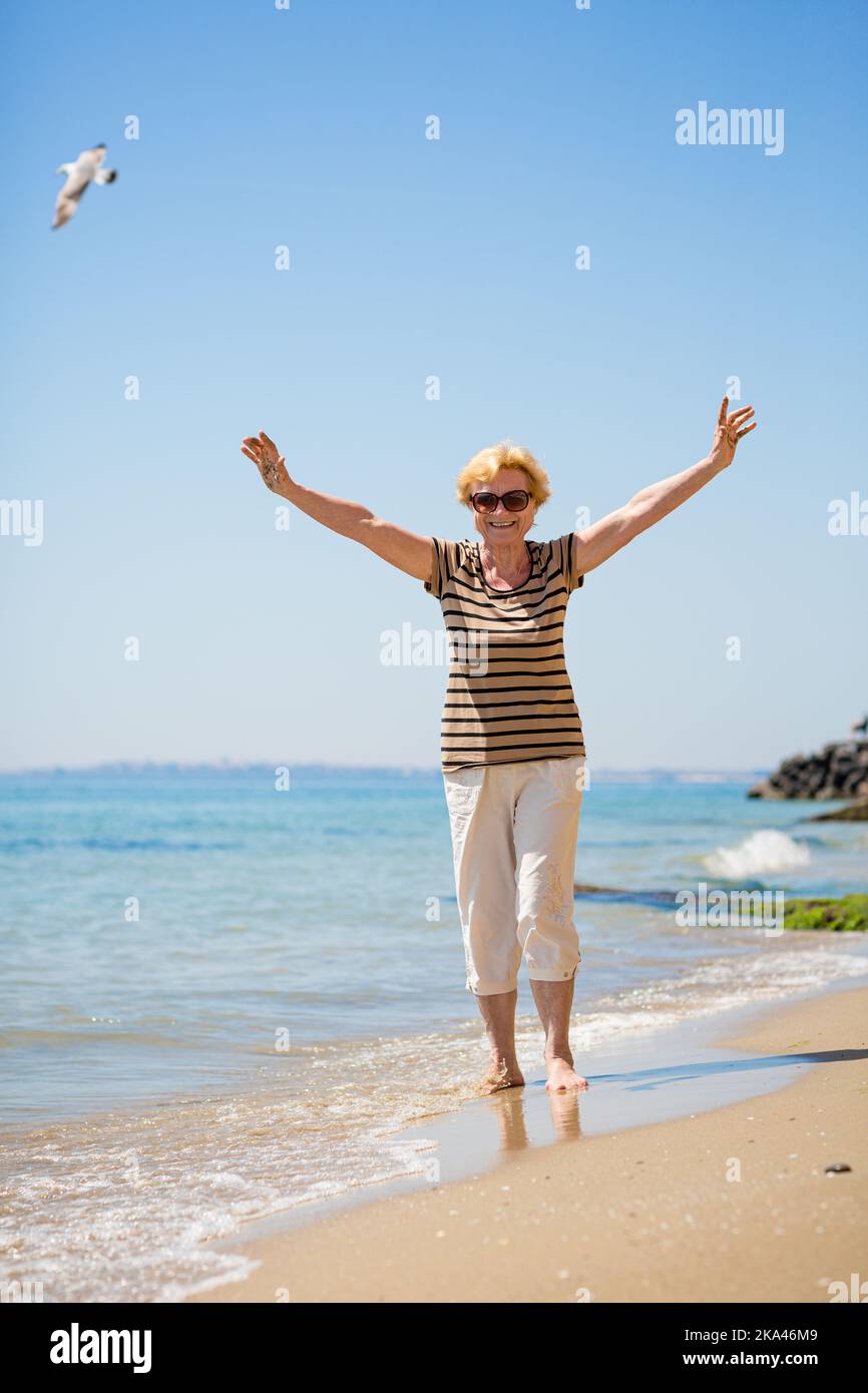 Ältere attraktive Frau, die am Strand entlang läuft und ihre Handflächen zeigt Stockfoto