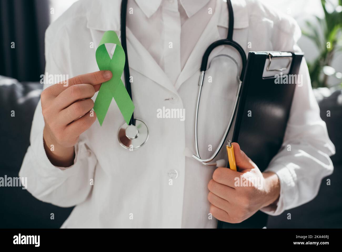 Nahaufnahme einer Ärztin in weißer Uniform mit Stethoskop mit Lime Green Ribbon und Clipboard sitzen auf der Couch, Bewusstsein für psychische Gesundheit und Organdon Stockfoto