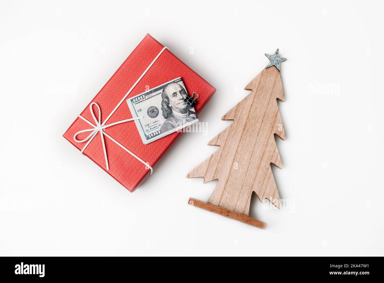 Ausgaben, Weihnachtsbudget und Sparkonzept. Weihnachts-Geschenkbox, Stapel von Dollarscheinen und hölzerner Weihnachtsbaum auf weißem Tisch Stockfoto