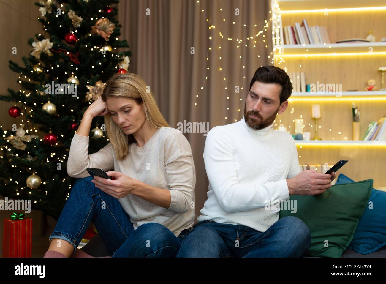 Das Familienpaar streitete sich an Weihnachten, saß zu Hause auf dem Sofa, Ehemann und Ehefrau sprachen nicht miteinander, hielten Telefone in den Händen, durchstöberten soziale Netzwerke, in der Nähe des Weihnachtsbaums. Stockfoto