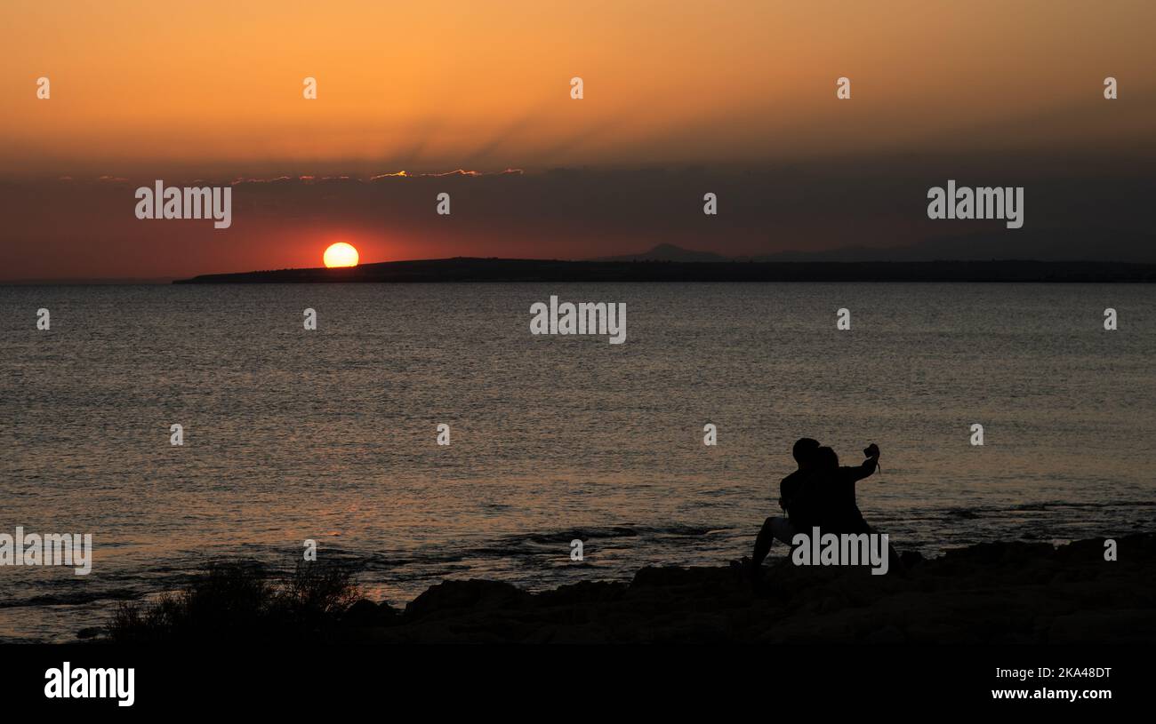 Silhouette eines jungen Paares, das den wunderschönen Sonnenuntergang am Strand genießt. Romantische Moment menschliche Beziehung Stockfoto
