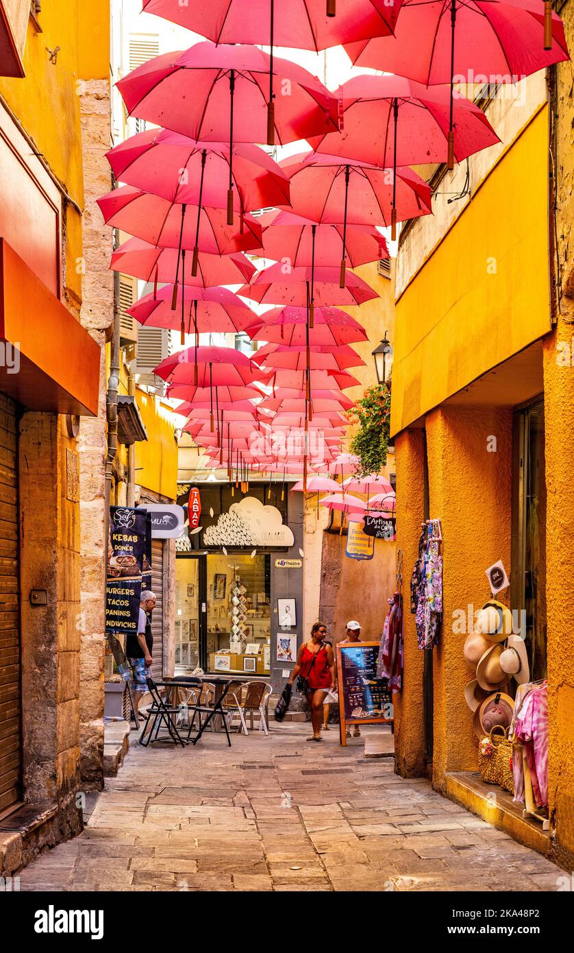 Grasse, Frankreich - 6. August 2022: Historische Mietshäuser und enge Straßen mit rosa Regenschirmen aus dem alten Stadtviertel der Parfümerie-Stadt Stockfoto