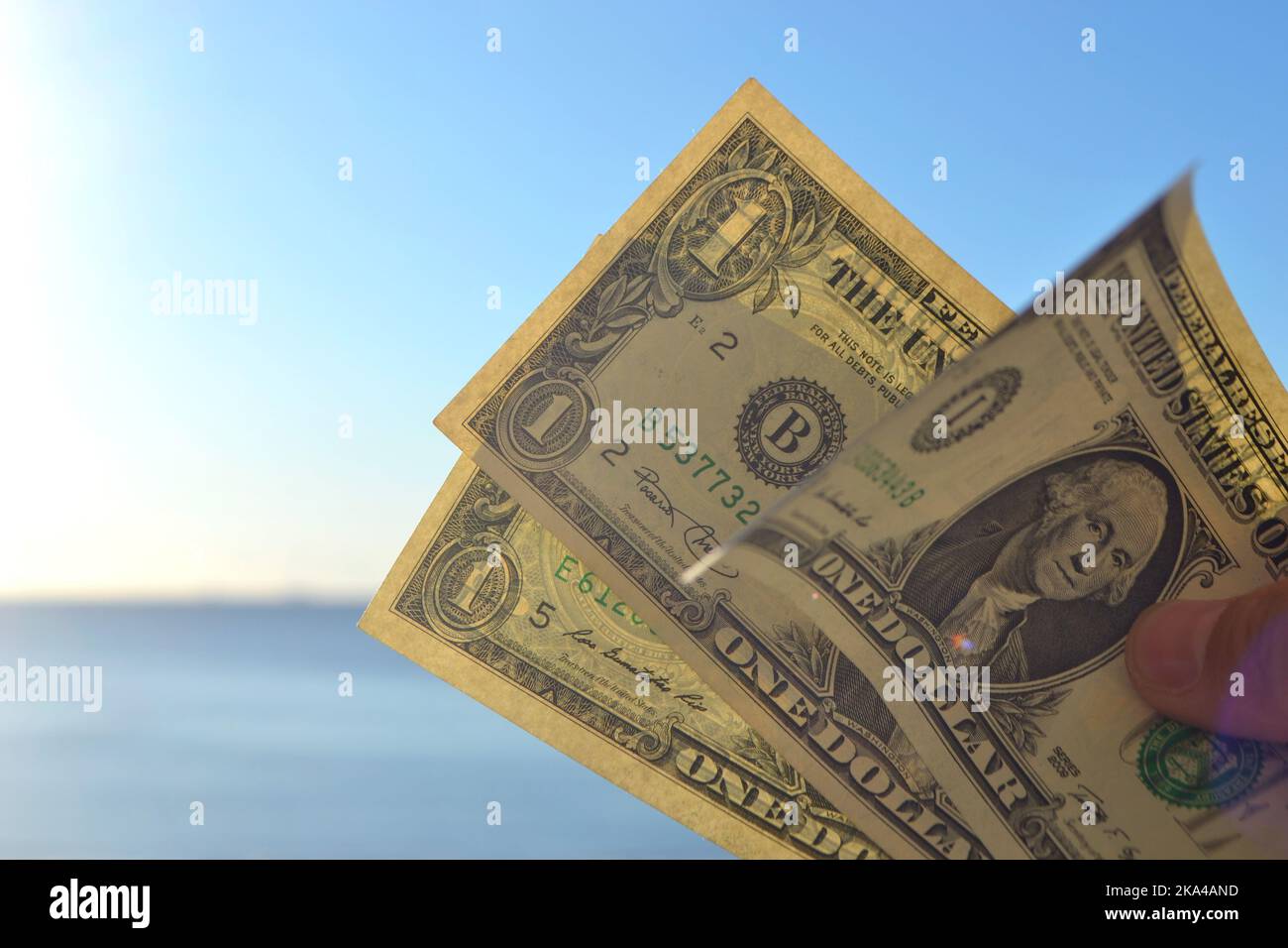 Mann hält drei ein-Dollar-Banknoten in der Hand vor dem Hintergrund des blauen Meeres und des blauen Himmels am sonnigen Sommertag. Das Konzept von Geld, Finanzen, Geld, Reisen, Tourismus, Urlaub, Erholung Stockfoto