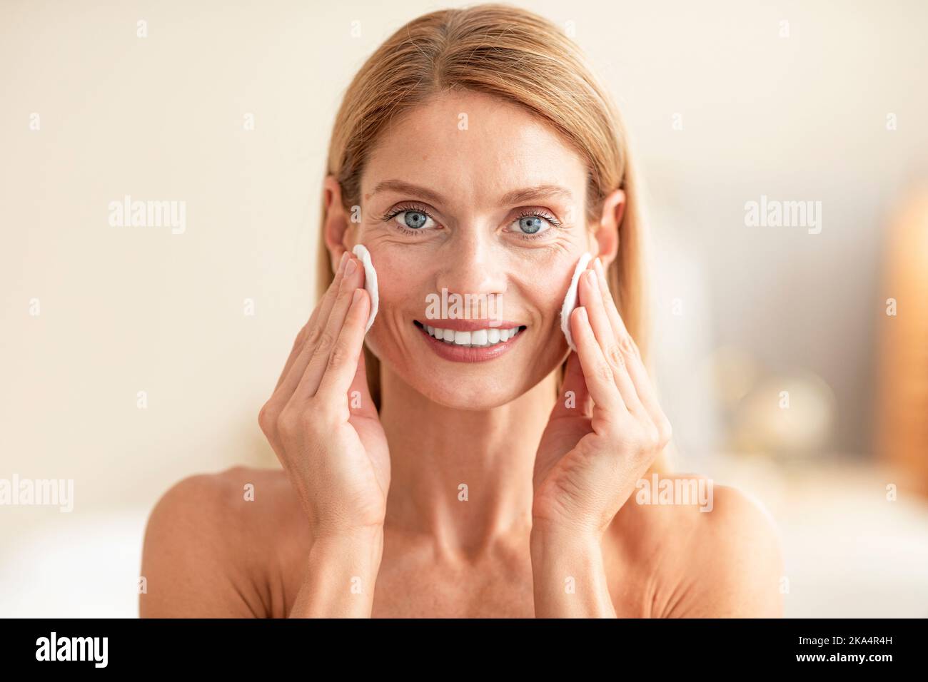 Porträt einer Frau mittleren Alters, die Wattepads verwendet, Make-up aus ihrem Gesicht löscht, Gesichtswasser auftragt oder Reinigungsmilch auftragt Stockfoto