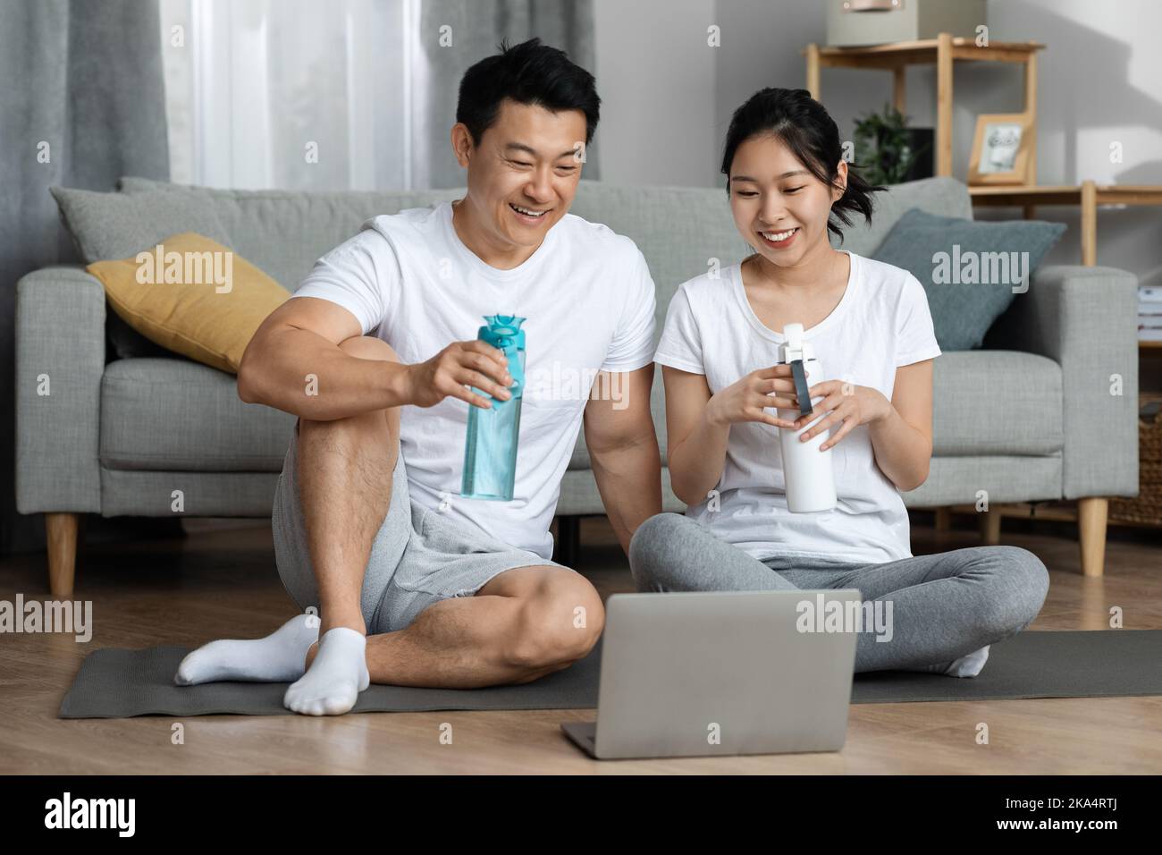 Fröhlicher chinesischer Mann und Frau, die nach dem Training Wasser trinken Stockfoto
