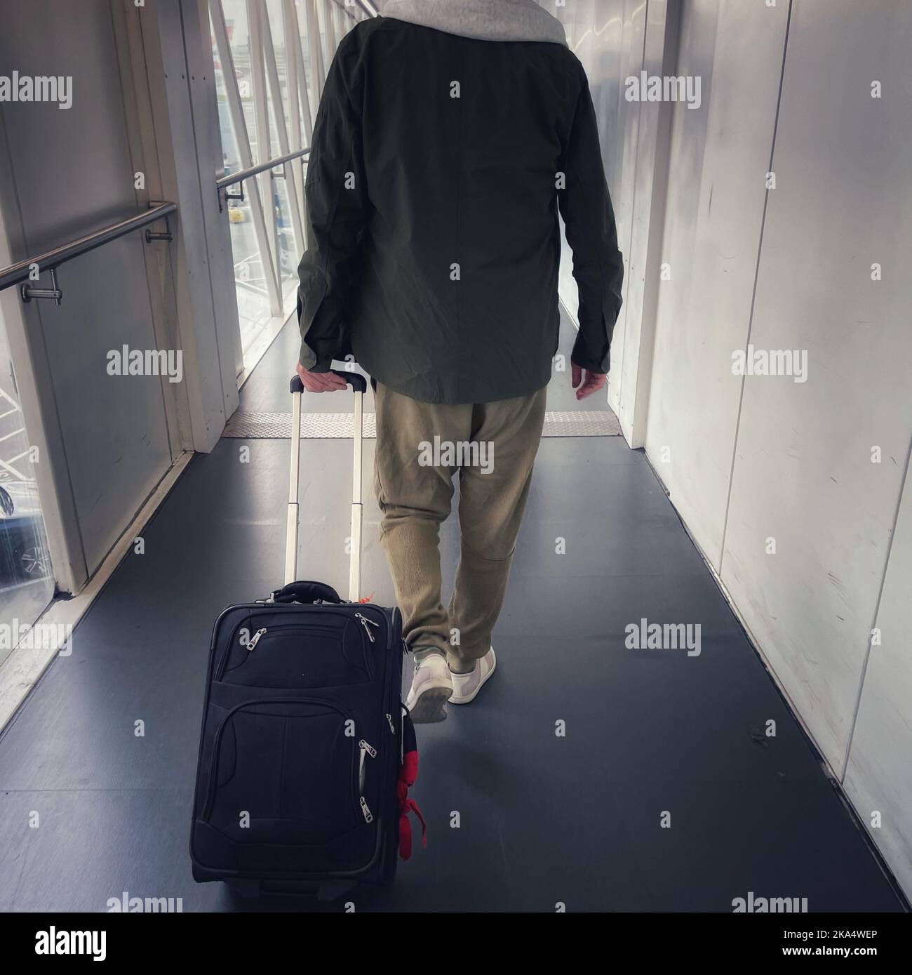 Rückansicht eines Mannes, der am Flughafen mit Gepäck auf Rädern den Korridor entlang läuft Stockfoto