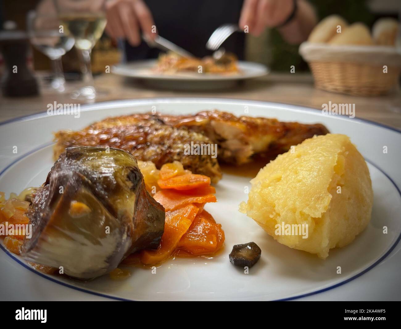 Nahaufnahme der Hähnchenbrust mit Kartoffeln, Artischocke und Karotte mit einer Person, die im Hintergrund isst Stockfoto