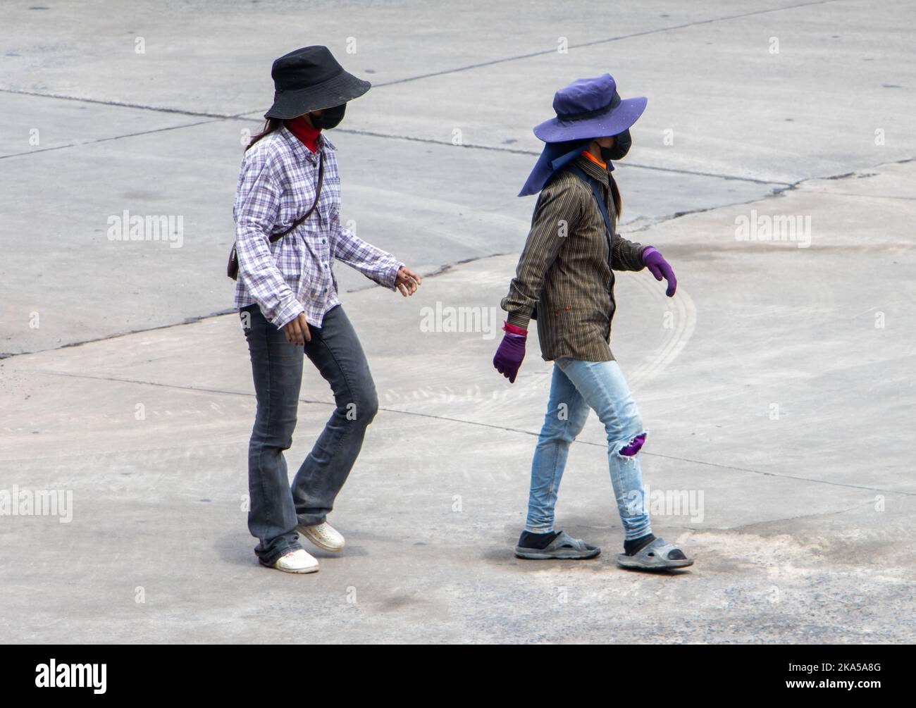 Zwei Bauarbeiterinnen mit verborgenen Gesichtern gehen eine sonnige Straße entlang, Thailand Stockfoto