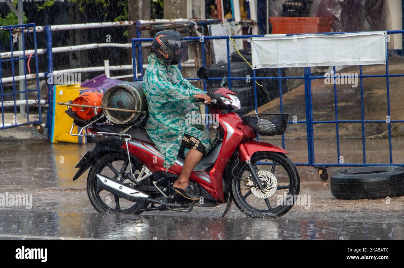 Ein Mann in einem Regenmantel trägt bei starkem Regen Gasflaschen auf einem Motorrad Stockfoto