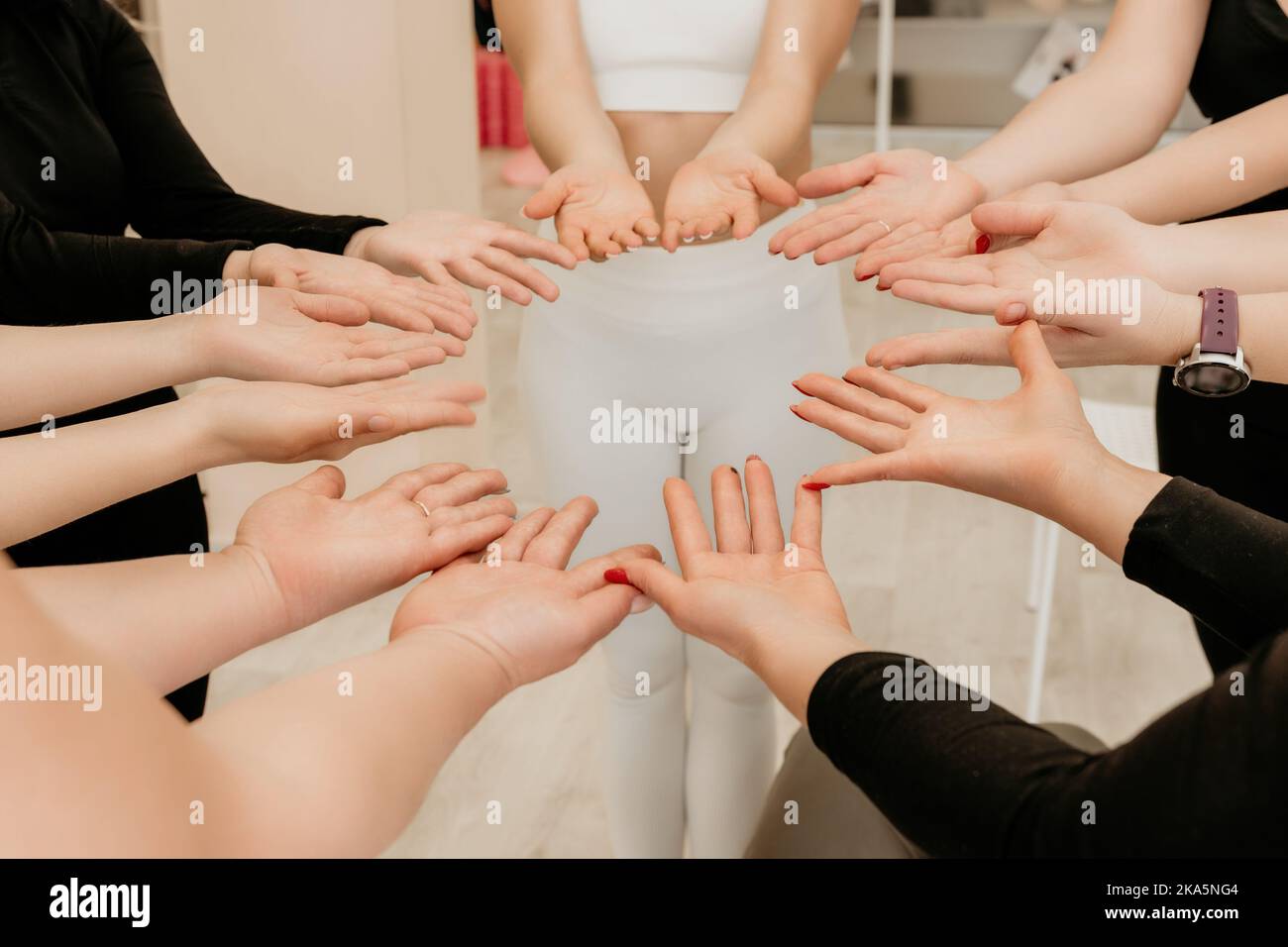 Partnerschafts- und Einheitskonzept: Unkenntliche Frauen in Sportbekleidung halten sich gegenseitig die Handgelenke und bilden einen Kreis. Eine Gruppe von jungen Frauen, die glücklich sind Stockfoto