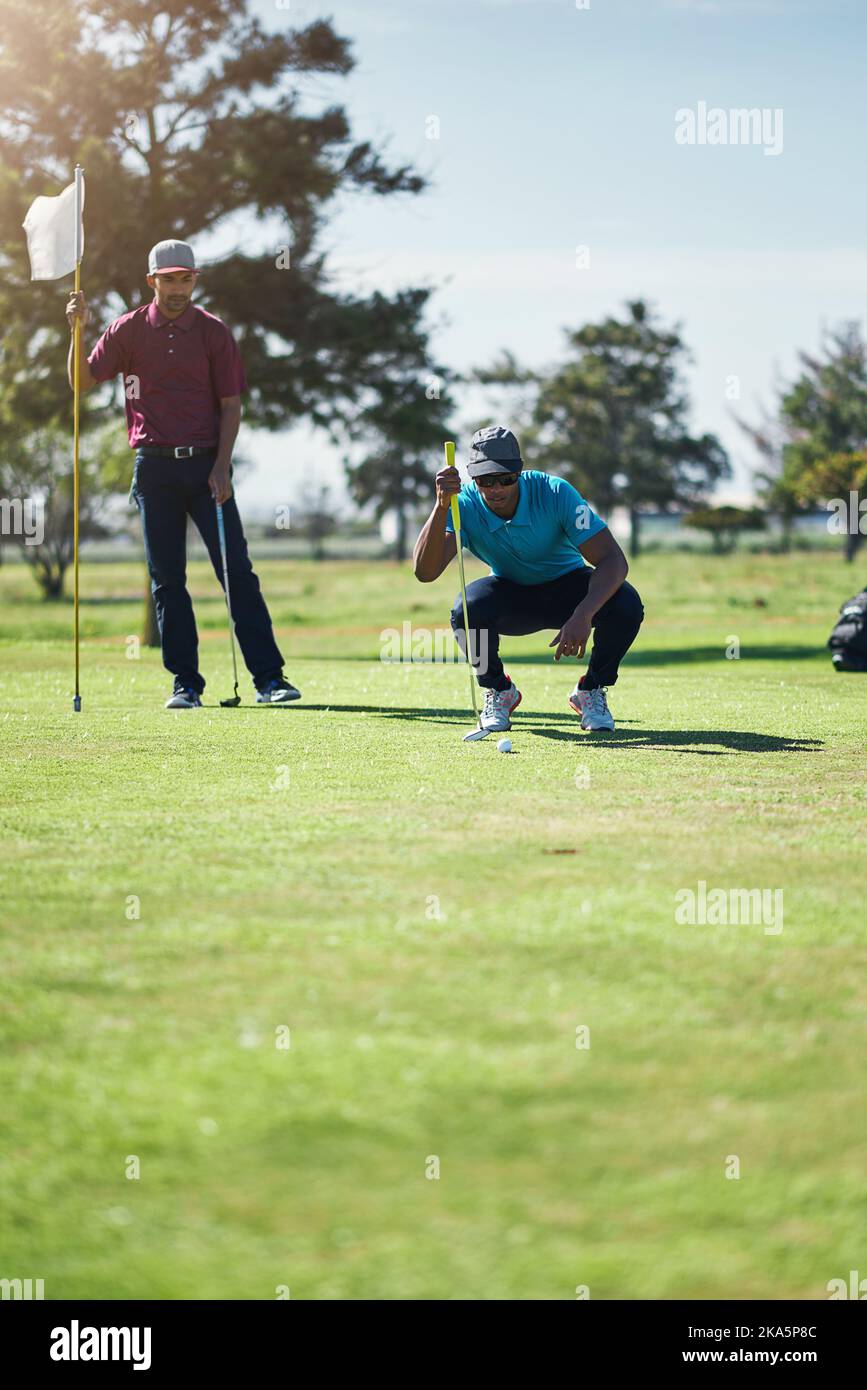 Schön gemacht. Ein fokussierter junger Golfer, der einen Golfball anschaut, während er tagsüber draußen auf dem Gras sitzt. Stockfoto