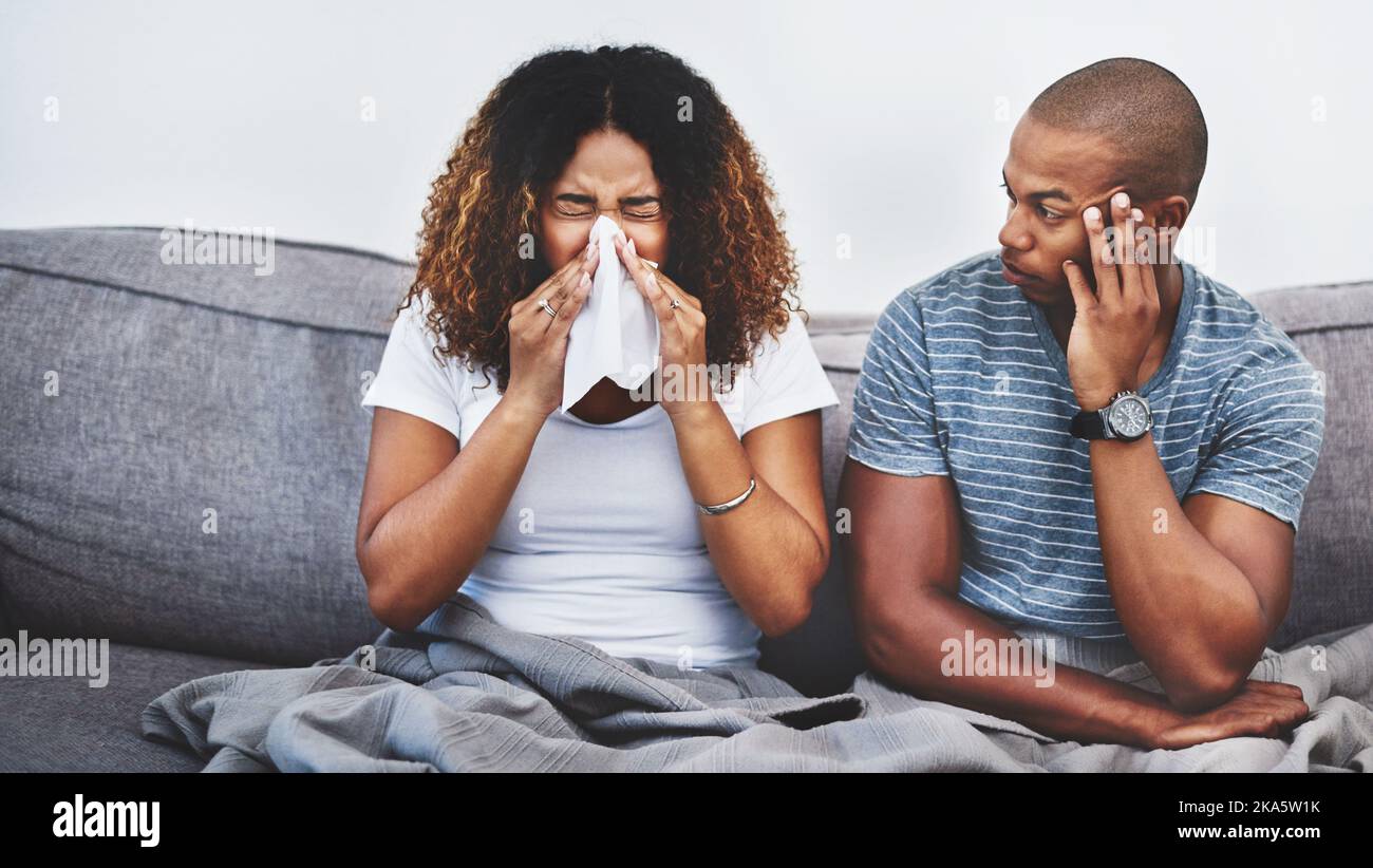 Wird Ihr Niesen jemals zu einem Ende kommen. Ein junger Mann, der von seiner Freundin, die zu Hause an Allergien leidet, geniert wird. Stockfoto
