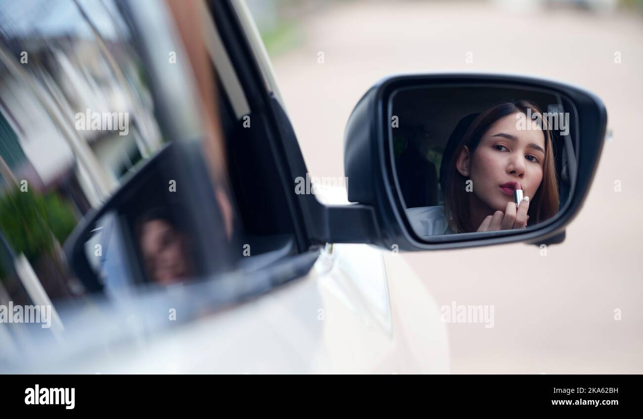 Junge Frau, die Lippenstift anwendet, und die Spiegelung im Autospiegel betrachtet. Stockfoto