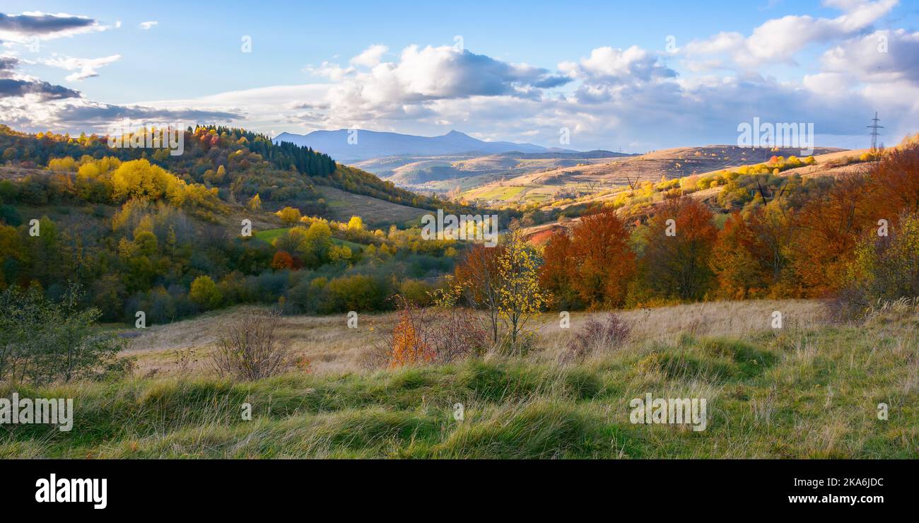 Herbstliche Landschaft der karpaten. Atemberaubende offene aussicht mit Dorf im Tal und hohen Gipfel in der Ferne unter einem Himmel mit flauschigen Wolken in Stockfoto