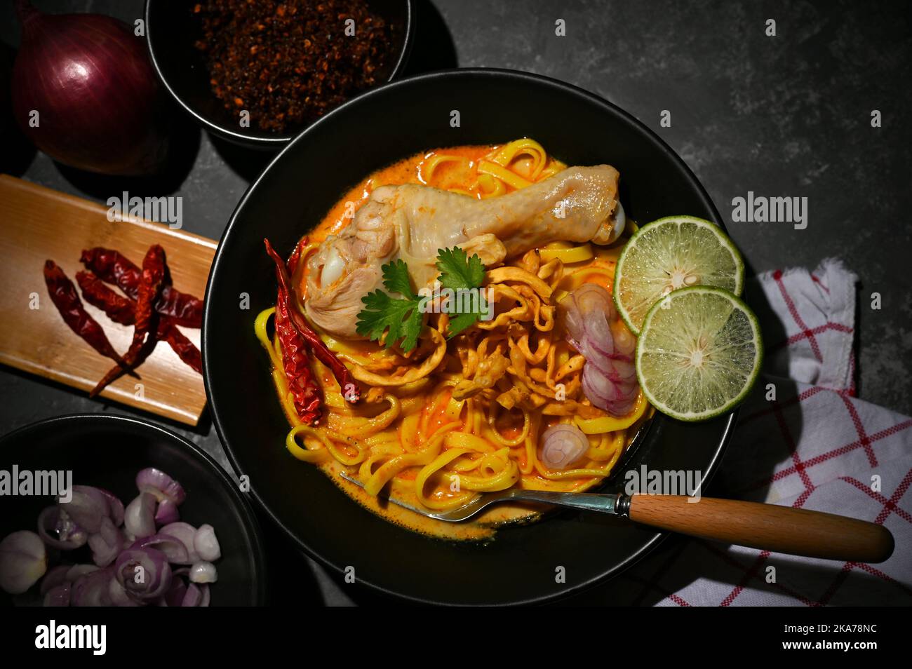 Blick von oben, Khao Soi Kai oder einzigartige nordthailändische Kursuppe mit Eiernudeln und Huhn auf einem schwarzen Esstisch. Thailändisches Essenskonzept Stockfoto