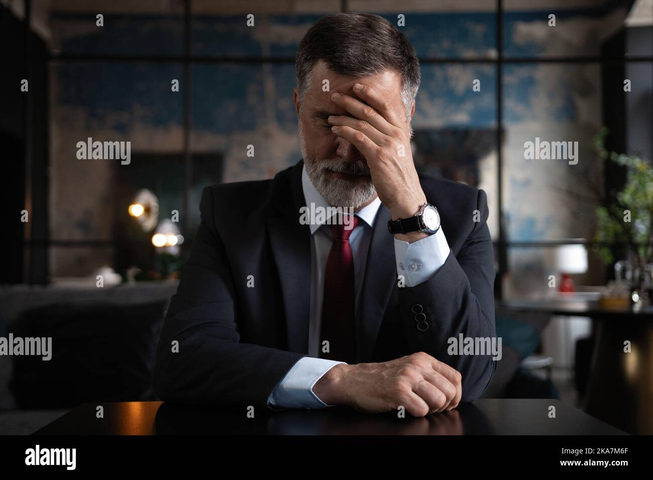 Frustrierter reifer Mann, der in einem modernen Büro sitzt. Überarbeiteter Geschäftsmann mit schrecklicher Migräne Stockfoto