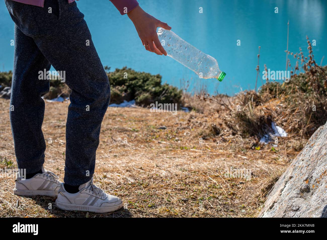 Zugeschnittenes Bild einer Frau, die in einem Naturschutzgebiet Müll aufsammelt. Unterer Teil des Körpers, bequeme Kleidung. Neben einem See. Stockfoto