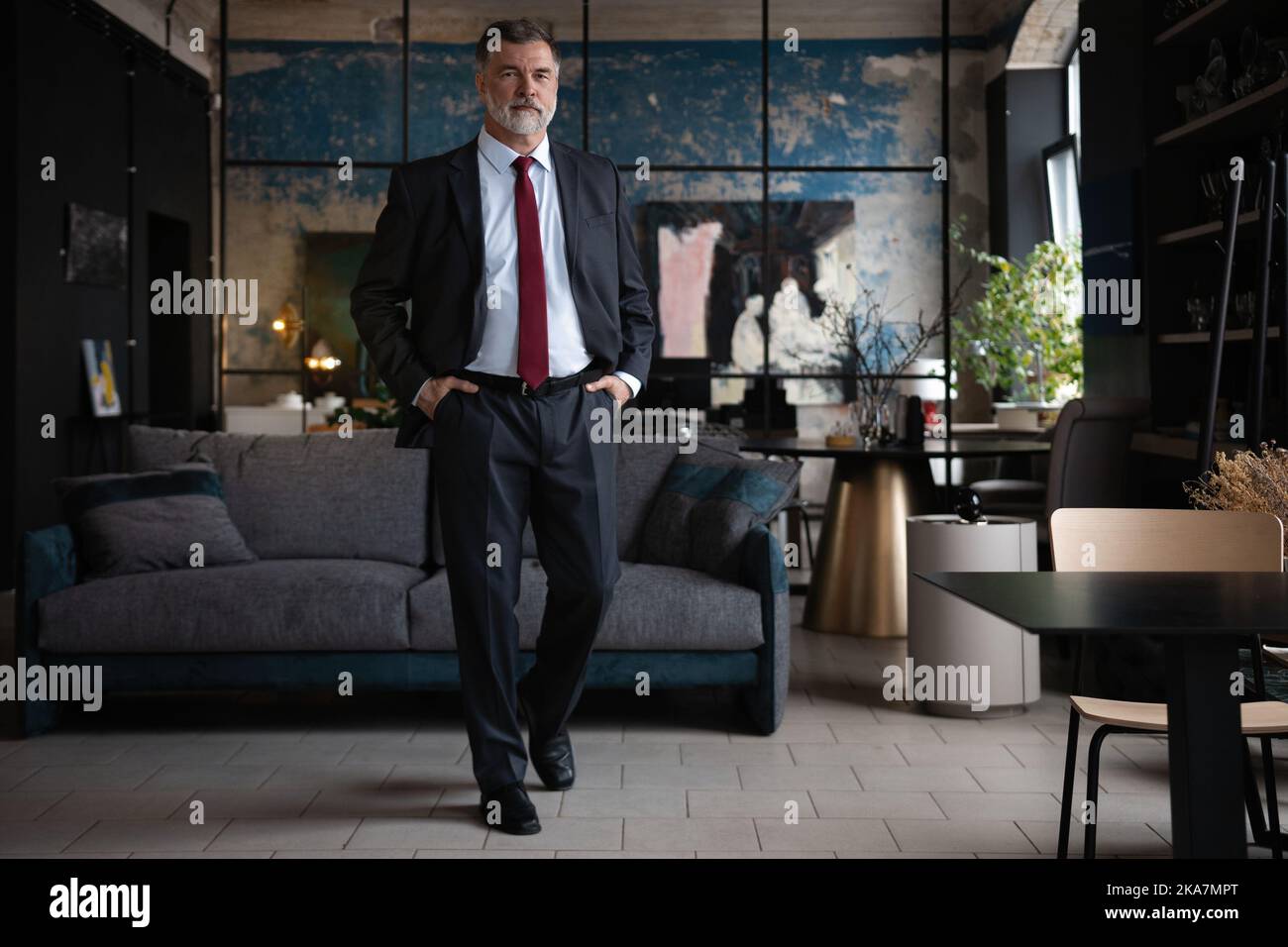 Erfolgskonzept. Stilvoller bärtiger Mann in einem Anzug, der im modernen Büro steht. Stockfoto