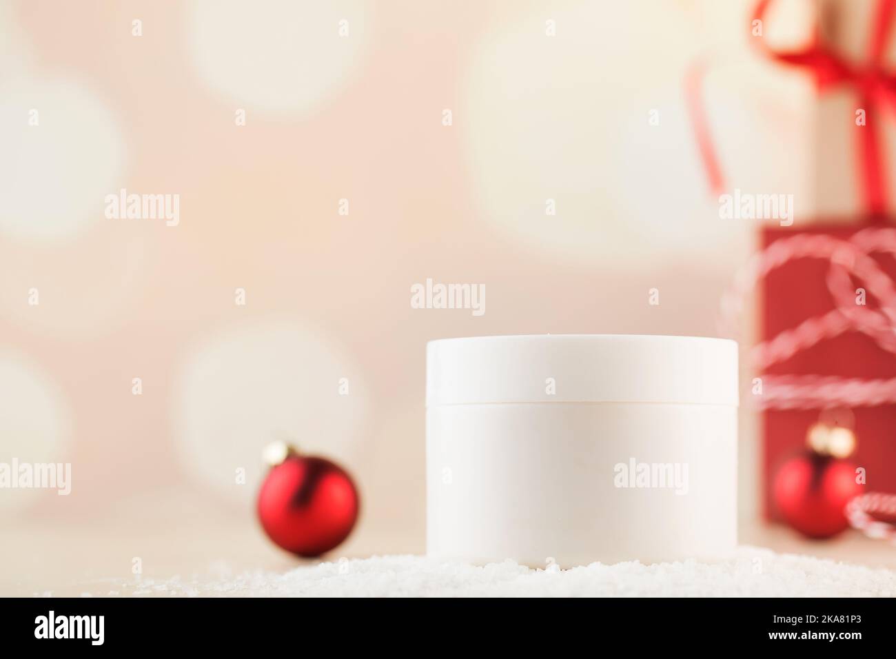 Ein weißes Glas mit pflegender Creme für Gesicht und Körper im Schnee mit Weihnachtskugeln Stockfoto