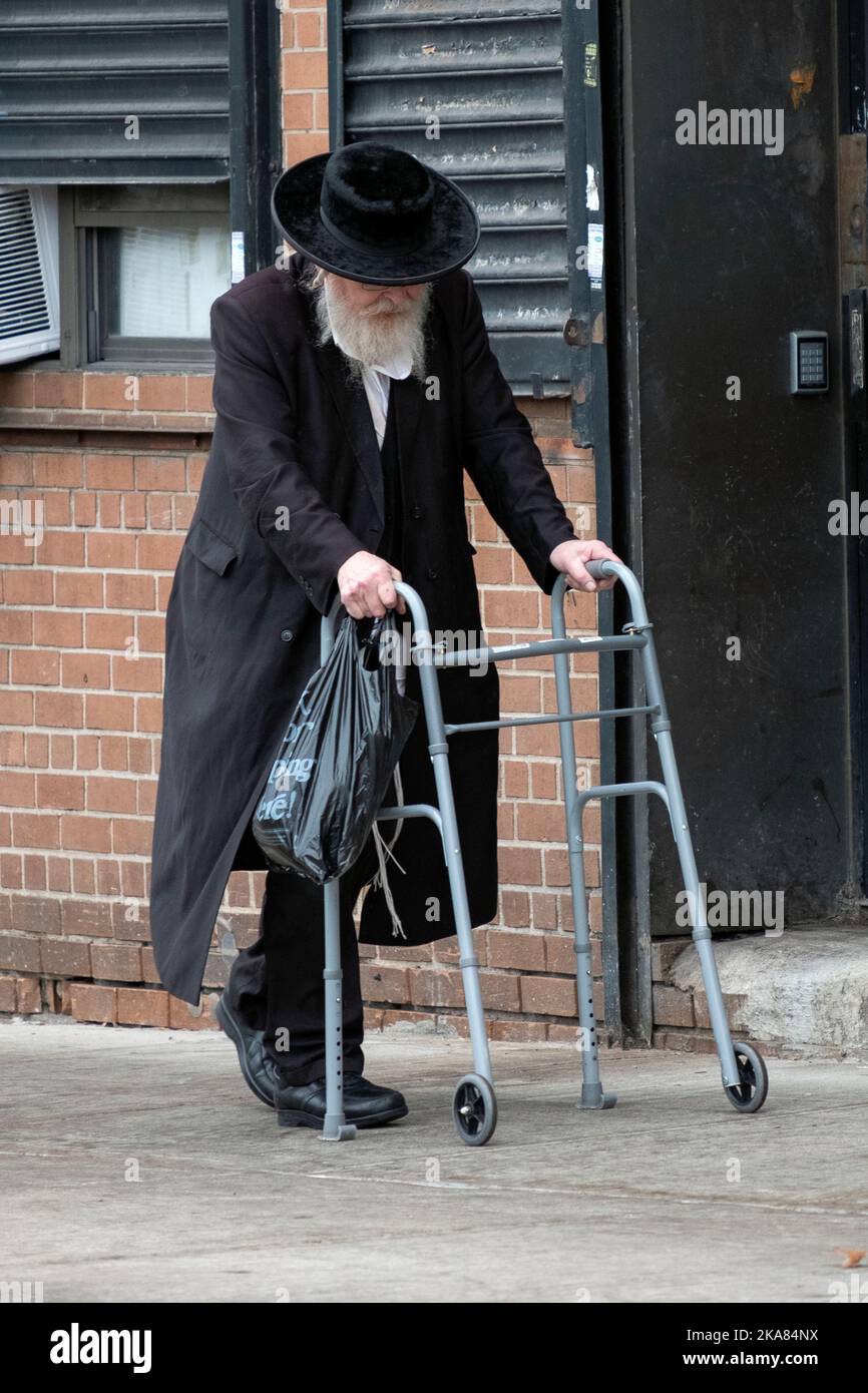 Ein älterer chassidischer Jude kehrt mit Hilfe eines Wanderers vom Einkaufen zurück. In Williamsburg, Brooklyn, New York City. Stockfoto