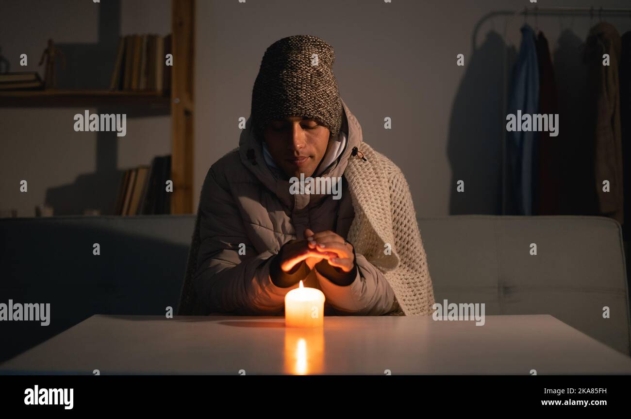 Junger Mann ohne Strom zu Hause mit Kerze. Abschaltung von Heizung und Strom, Stromausfall, Stromausfall, Lastverfall oder Energiekrise Stockfoto