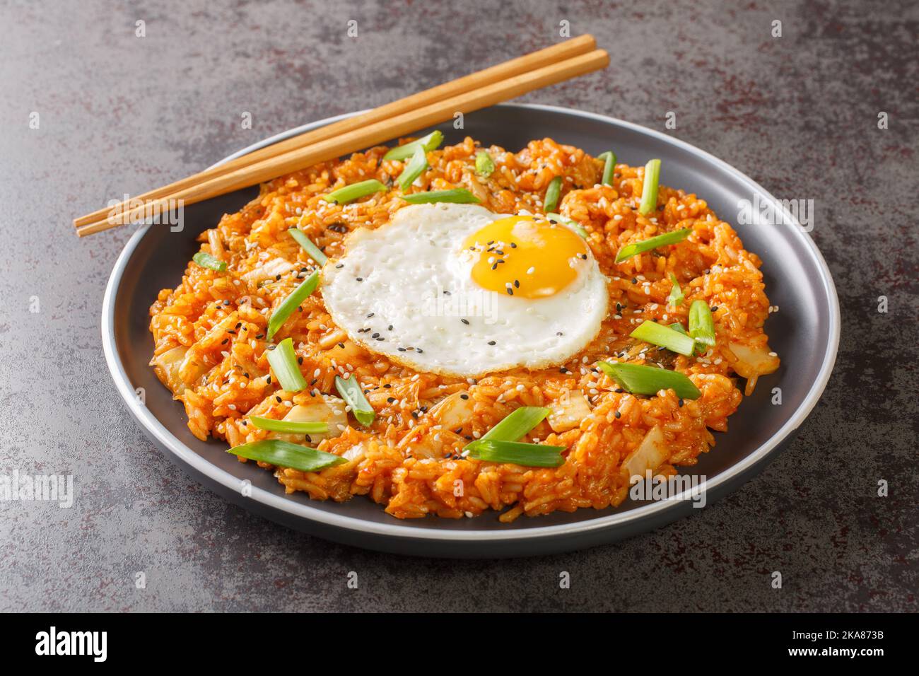 Koreanischer Kimchi gebratener Reis mit Ei, grüner Zwiebel und Sesam in Nahaufnahme auf einem Teller auf dem Tisch. Horizontal Stockfoto