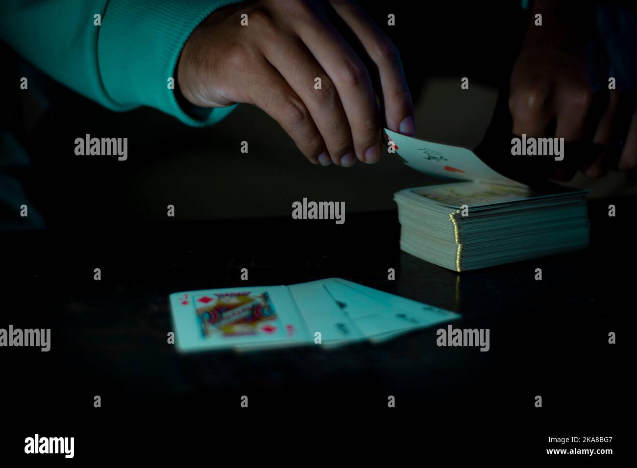 Ein Mann, der mit Karten auf einem Tisch in einem dunklen Hintergrund spielt Stockfoto