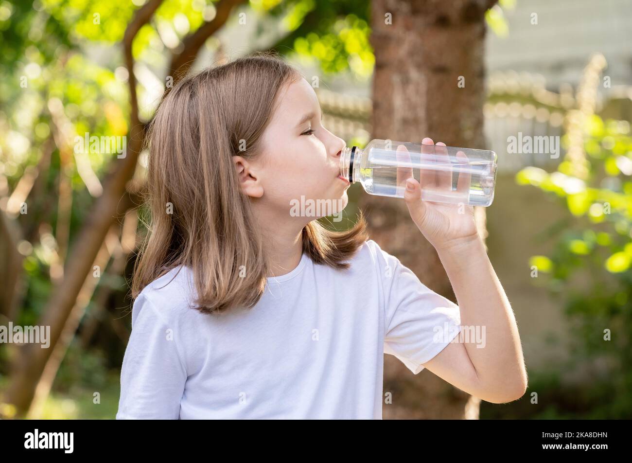 Grundschulalter Kind, Mädchen trinken frisches sauberes klares gefiltertes Wasser aus einer wiederverwendbaren transparenten Plastikflasche im Freien Porträt eine Person CH Stockfoto