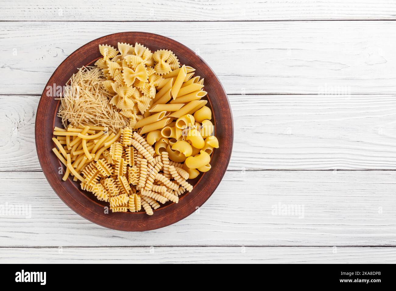 Verschiedene Arten und Formen der italienischen Pasta in Keramik-Platte auf weißem Holzhintergrund mit Kopie Spase Stockfoto