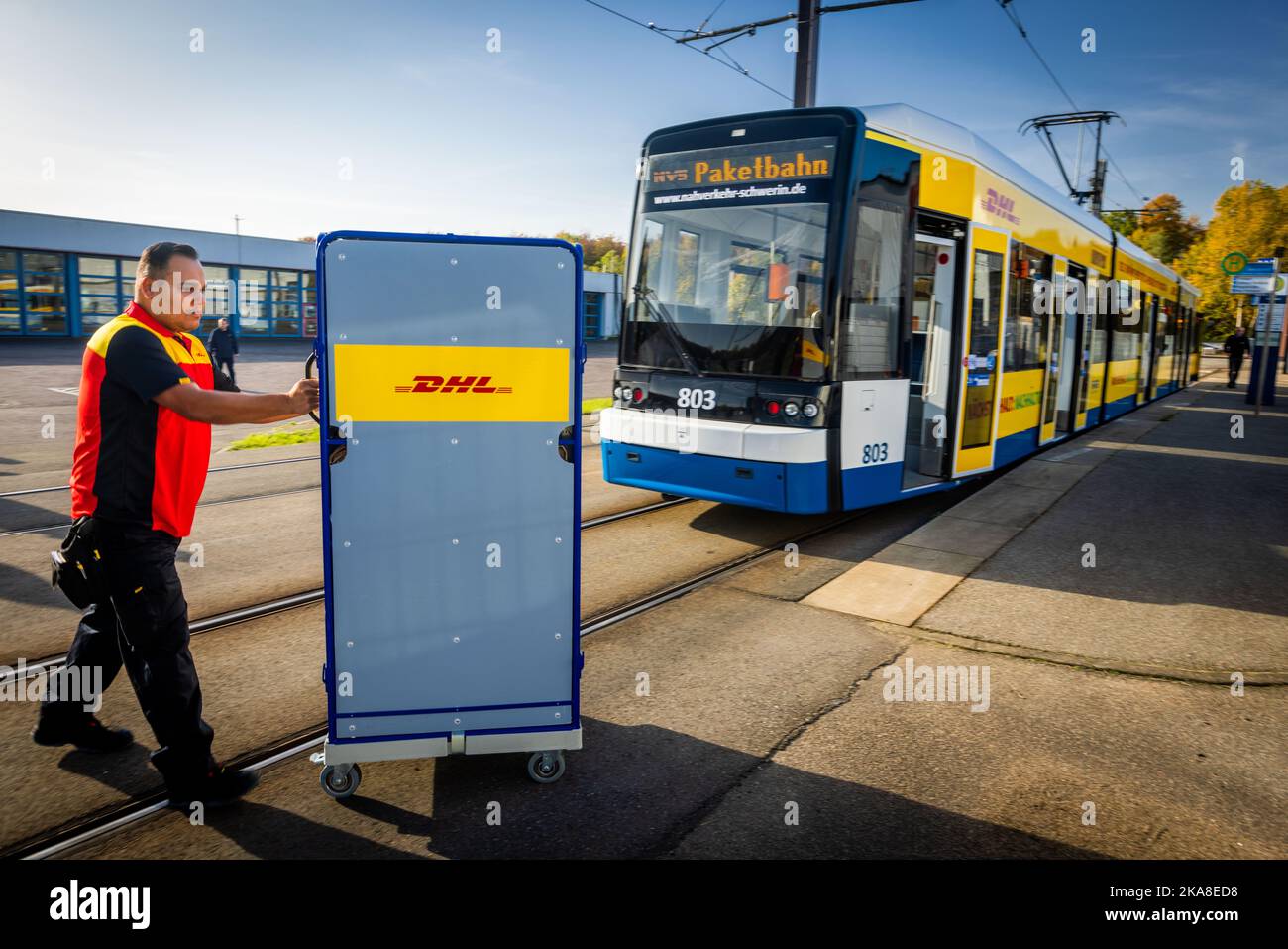 Schwerin, Deutschland. 28. Oktober 2022. Ein Mitarbeiter der Deutschen Post  schiebt einen Transportwagen für Pakete in eine Straßenbahn des Schweriner  ÖPNV. Die Deutsche Post hat ein Pilotprojekt zur Paketzustellung mit der  Straßenbahn