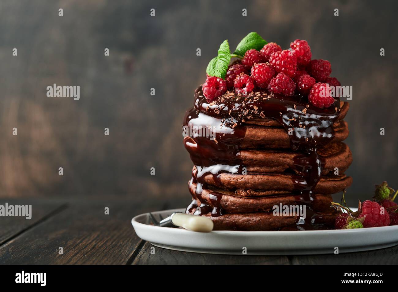 Schokoladenpfannkuchen. Pfannkuchen mit frischer Himbeere mit Schokoladenglasur oder Toppings in grauer Schale auf altem Holztischhintergrund. Hausgemachter Klassiker ameri Stockfoto