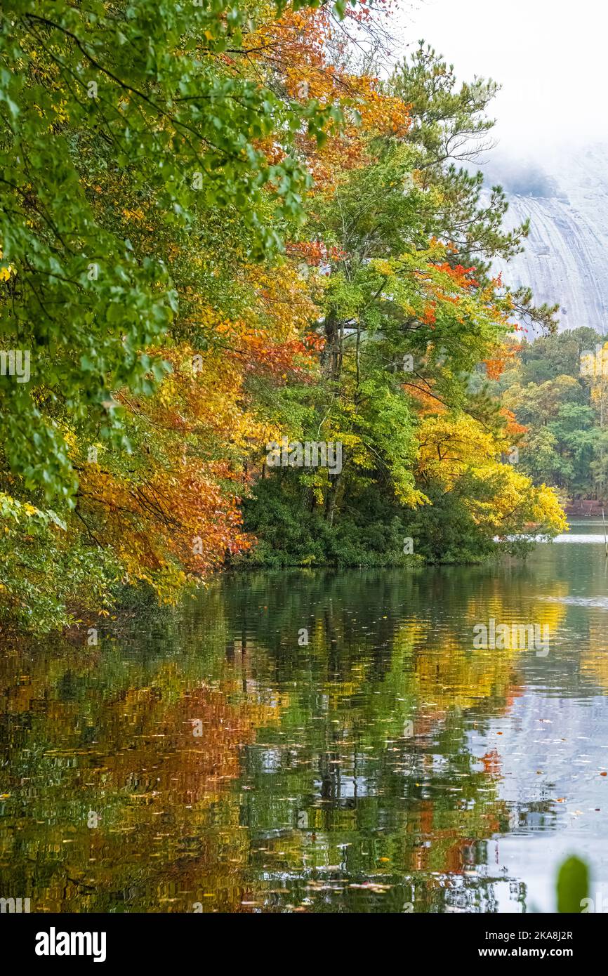 Lebendige Herbstfarben spiegeln sich in einem stillen See mit dem nebelbedeckten Granit von Stone Mountain im Hintergrund im Stone Mountain Park in Atlanta wider. Stockfoto