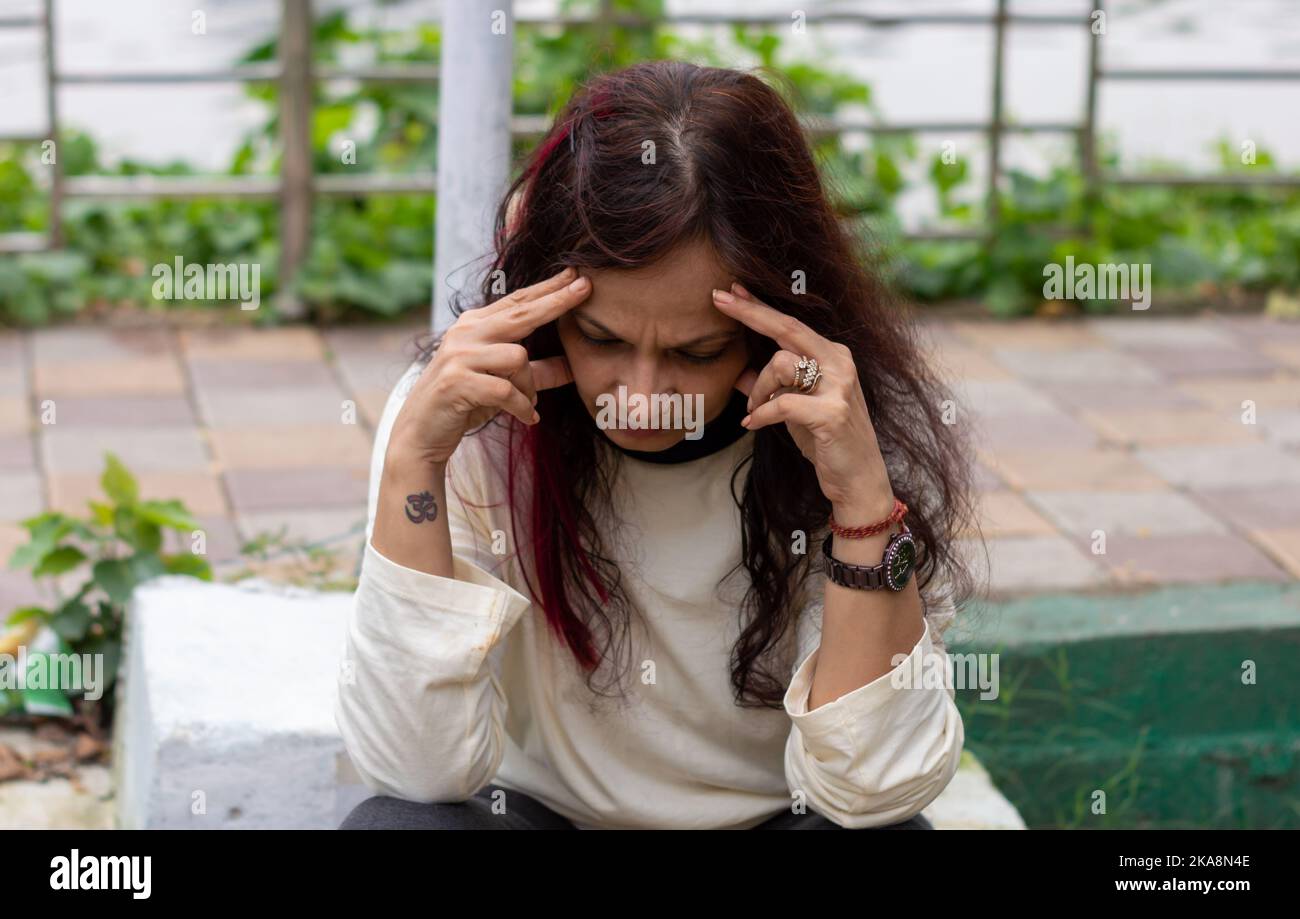 Deprimiert besorgt Frau sitzt in Stress-Pose in einer Parkbank und schaut Kopf nach unten Haltung. Vorderansicht. Indische Ethnizität Alter 50 bis 54 Jahre. Stockfoto