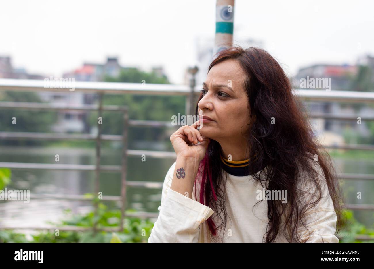 Mid Adult Sorgen Frau sitzt auf der Hand auf dem Kinn Pose in einer Parkbank und Blick auf eine Entfernung. Vorderansicht. Indische Ethnizität Alter 50 bis 54 Jahre. Stockfoto