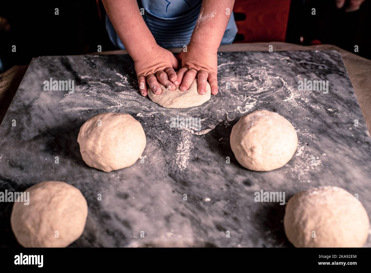 Ein Foto über dem Kopf von Kinderhände, etwas besprühtes Mehl und Weizenteig auf dem Marmortisch. Kinderhände machen den Teig für Pizza. Kleines Kind coo Stockfoto