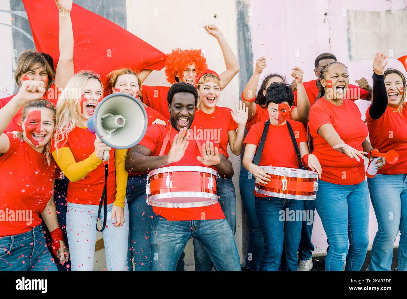Eine Gruppe glücklicher junger multiethnischer Fans jubelt ihr Team mit Fahnen, Megaphonen und Trommeln an Stockfoto