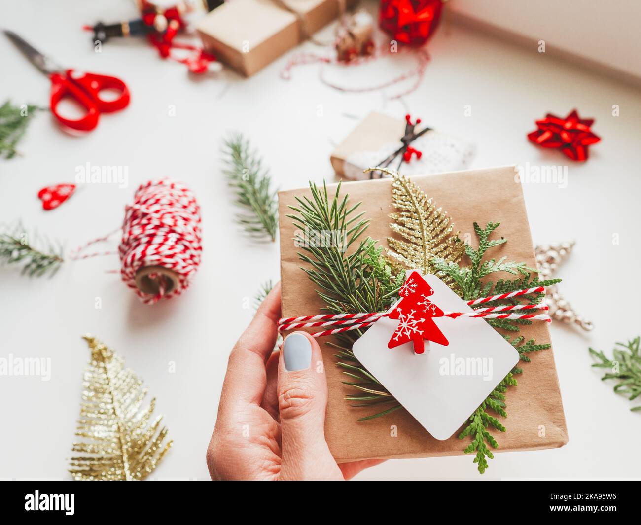 DIY-Geschenke verpackt in Bastelpapier mit Tannenzweigen und rotem Symbol des Weihnachtsbaums. Draufsicht auf Dekorationen zu Neujahrsgeschenken. Festlich Stockfoto